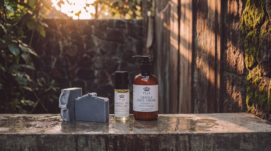 Peace Love & Soap Face collection featuring face cream, face serum, facial oil roll-on, and one unwrapped Charcoal Detox soap bar in a moody garden setting