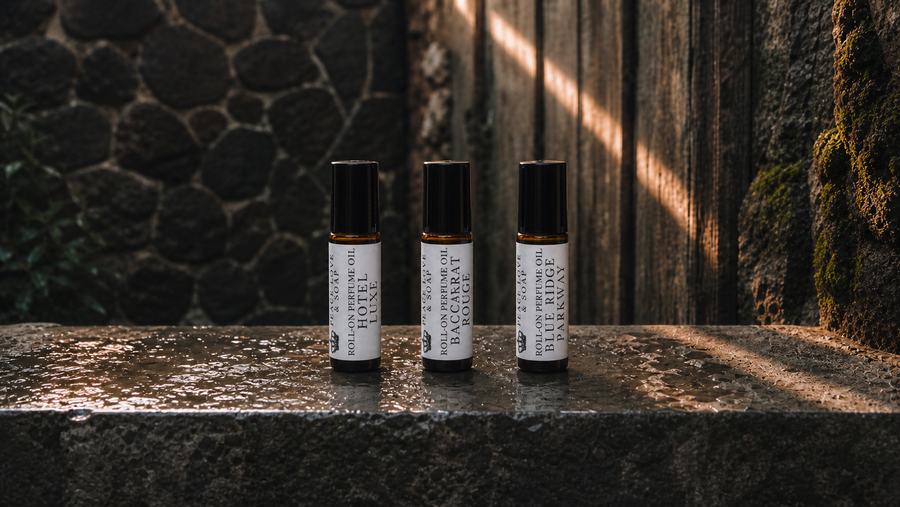 Three capped Peace Love & Soap perfume roll-ons standing upright on wet stone