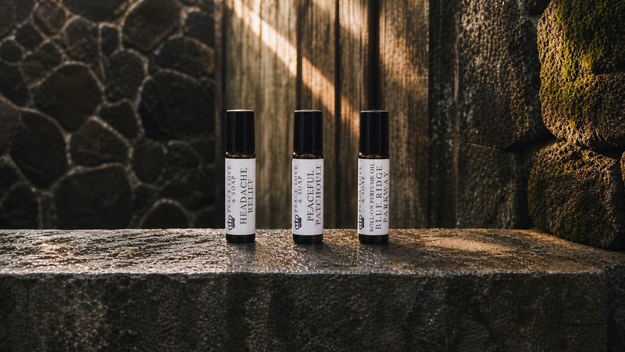 Three capped Peace Love & Soap roll-on oils standing upright on wet stone
