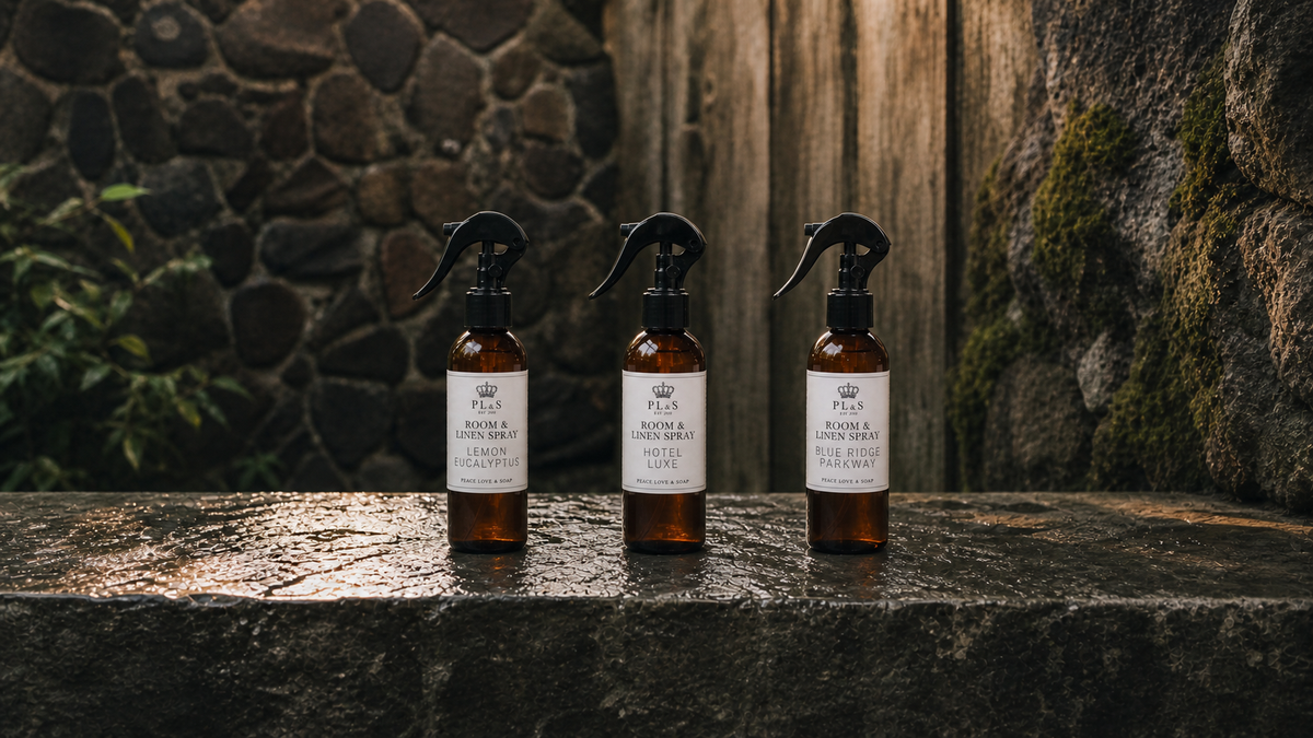 Peace Love & Soap room and linen sprays with clear labels on wet stone in a garden courtyard