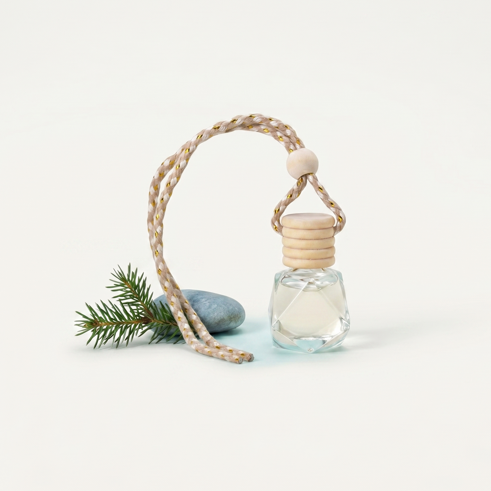 Small glass bottle with wooden cap on a string, next to a pine branch on a light background