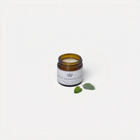 a small glass jar with a white label next to a green leaf