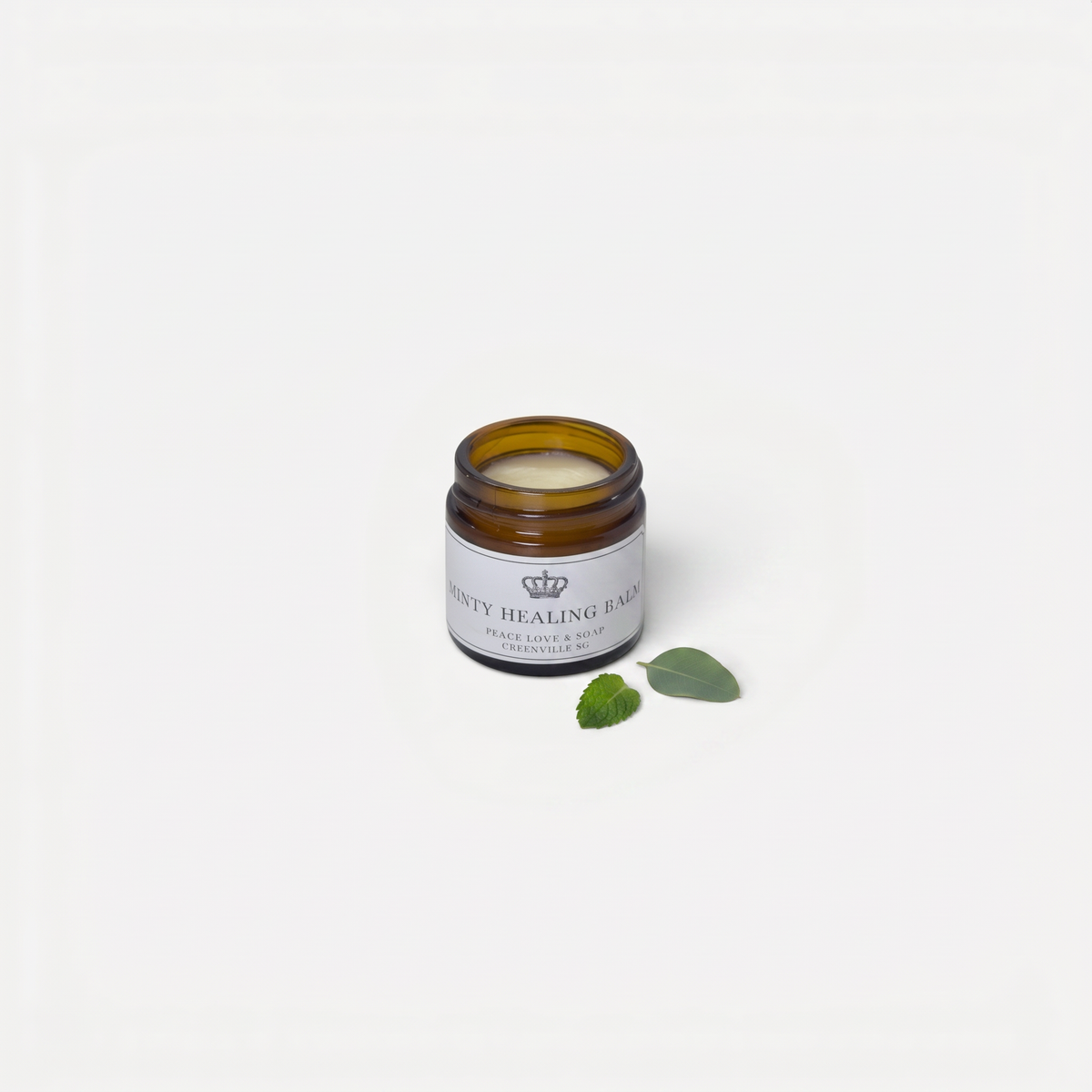 a small glass jar with a white label next to a green leaf