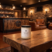 a white candle on a wooden table in a room with a stone fireplace and chairs